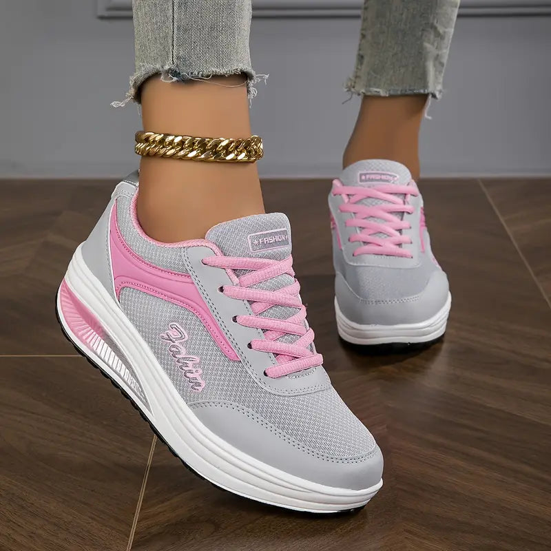 Chaussures plates pour femme Wanda tendance, baskets basses grises en mesh avec détails et lacets roses, semelle épaisse blanche confortable, portées avec un jean sur sol en bois.