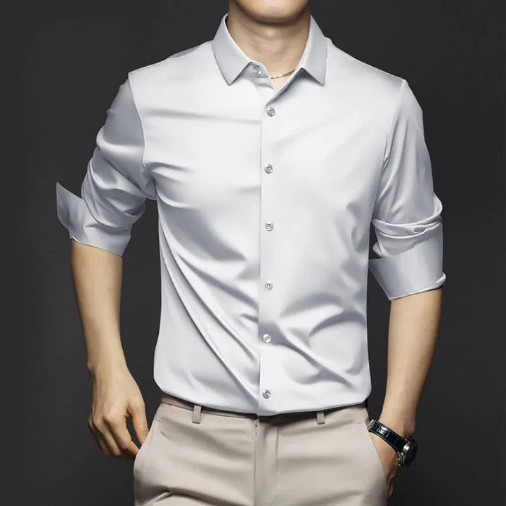 Chemise d’été Wulfric pour homme, blanche moderne à manches longues retroussées et boutonnée, coupe élégante portée avec pantalon beige.