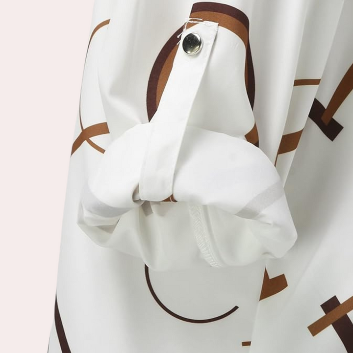 Gros plan sur la manche de la chemise femme Xavine avec motif de lettres graphiques marron. Détail de manche retroussable avec patte boutonnée, offrant un style moderne, élégant et pratique.