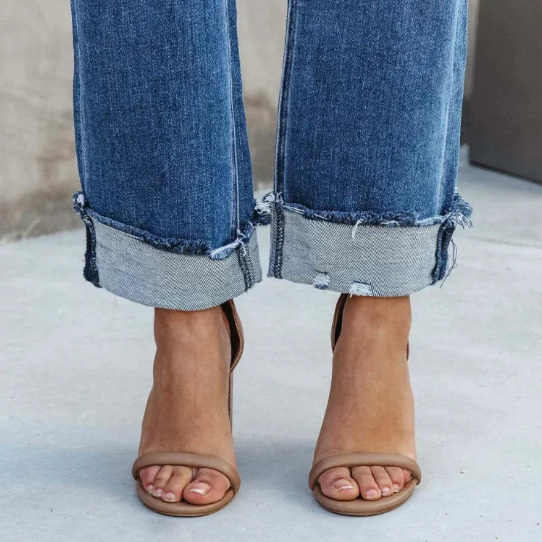 Gros plan du pantalon droit Zephyra pour femme bas de jean bleu coupe droite avec ourlets retroussés et finitions effilochées, porté avec des sandales à talons  détail moderne et tendance.