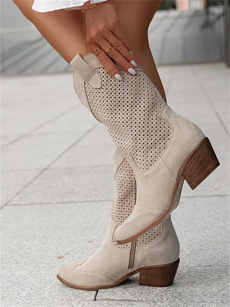 Une paire de bottes western mi-longues pour femme en daim beige clair, dotées d’un design perforé respirant et d’un petit talon carré en bois. Le modèle présente une coupe élégante et confortable, idéale pour un look tendance et décontracté. Photographiées sur une surface urbaine claire, ces bottes ajoutent une touche chic et moderne à une tenue estivale ou printanière.