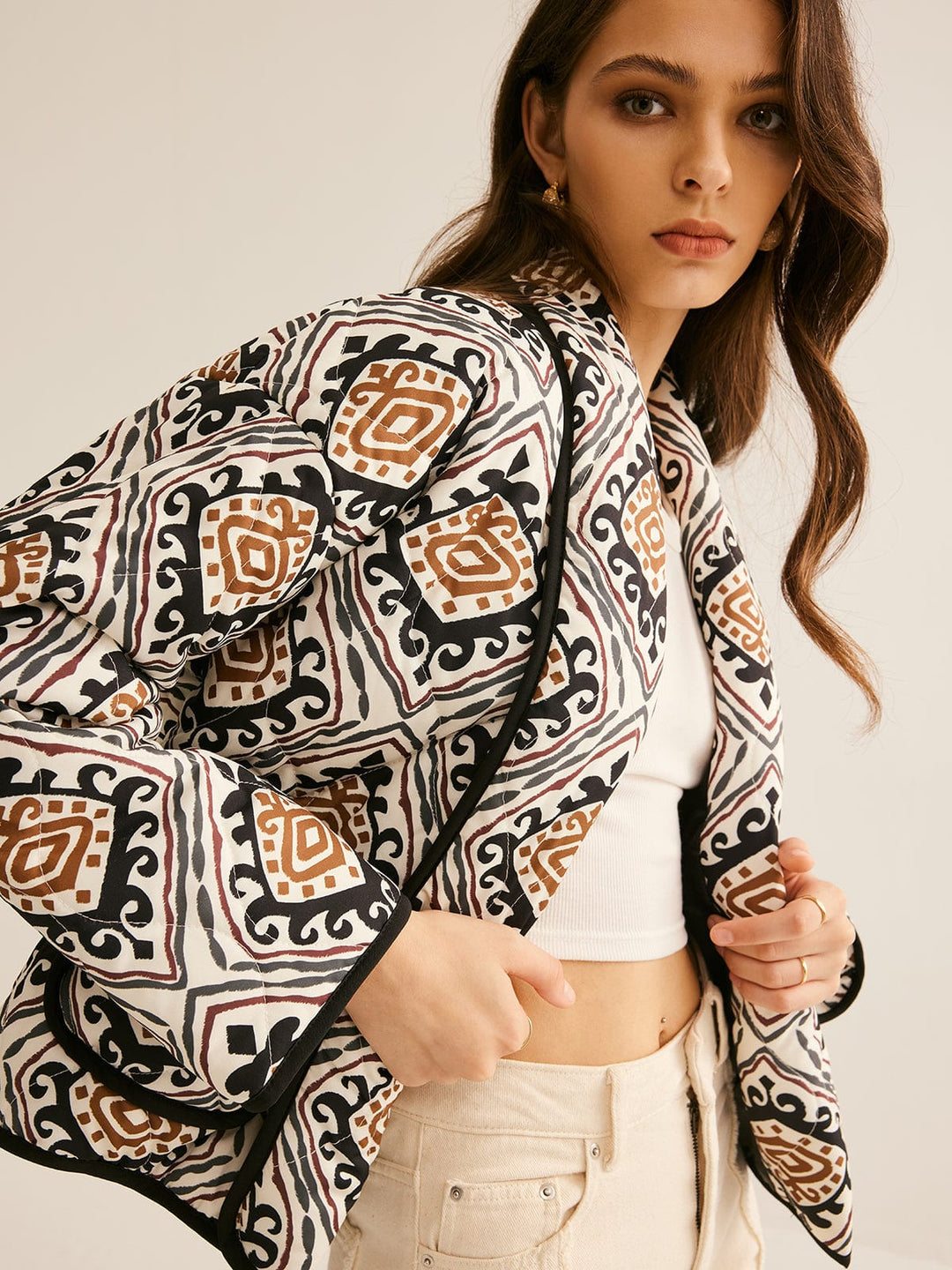 veste ample imprimée de motifs géométriques noirs, blancs et bruns, manches longues et bordure noire, portée ouverte sur un haut clair et un pantalon clair dans un cadre neutre, style moderne.
