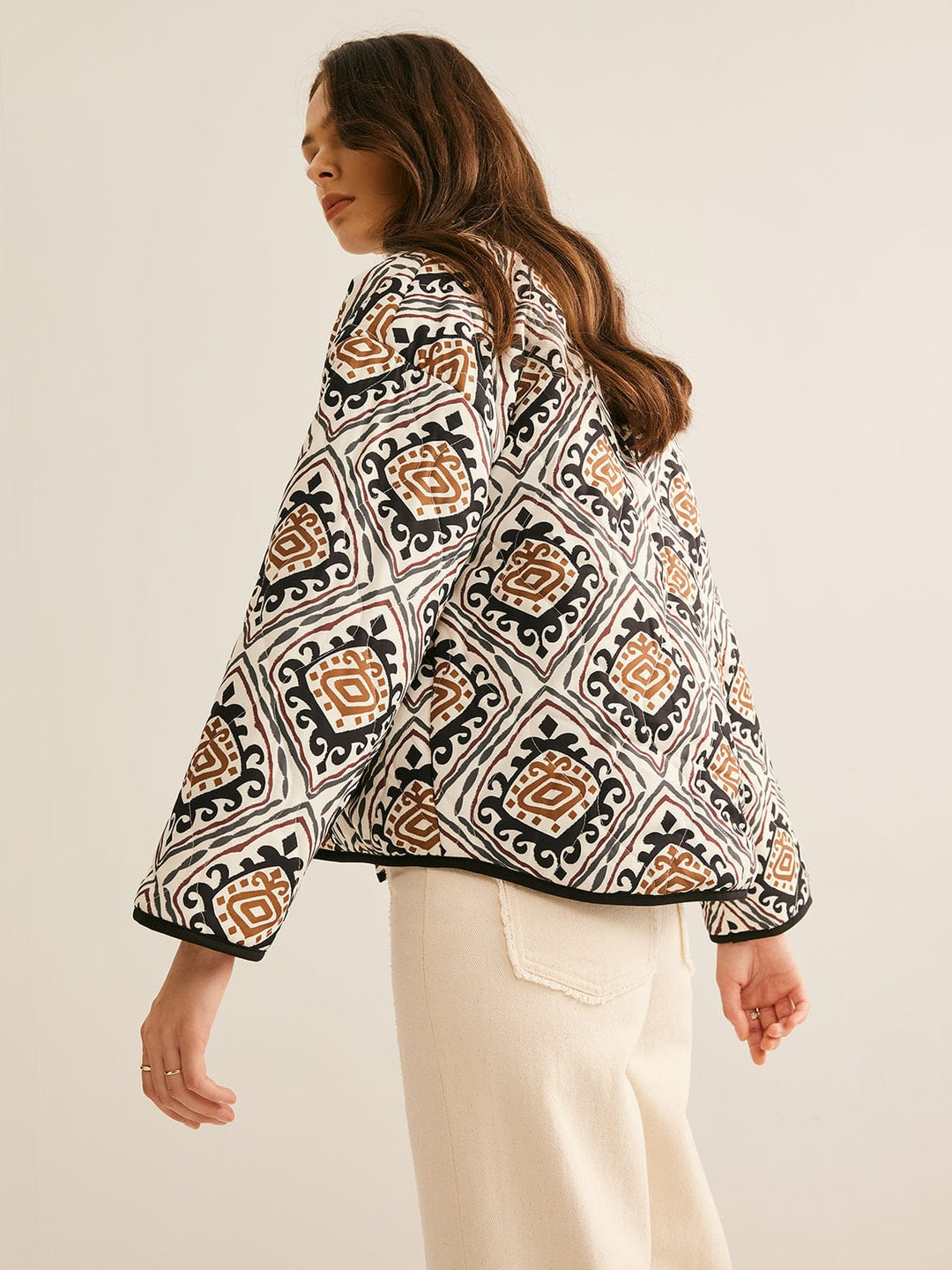 veste ample imprimée de motifs géométriques noirs, blancs et bruns, manches longues légèrement bouffantes et bordure noire, portée ouverte sur un haut clair et un pantalon clair dans un cadre neutre, style moderne.