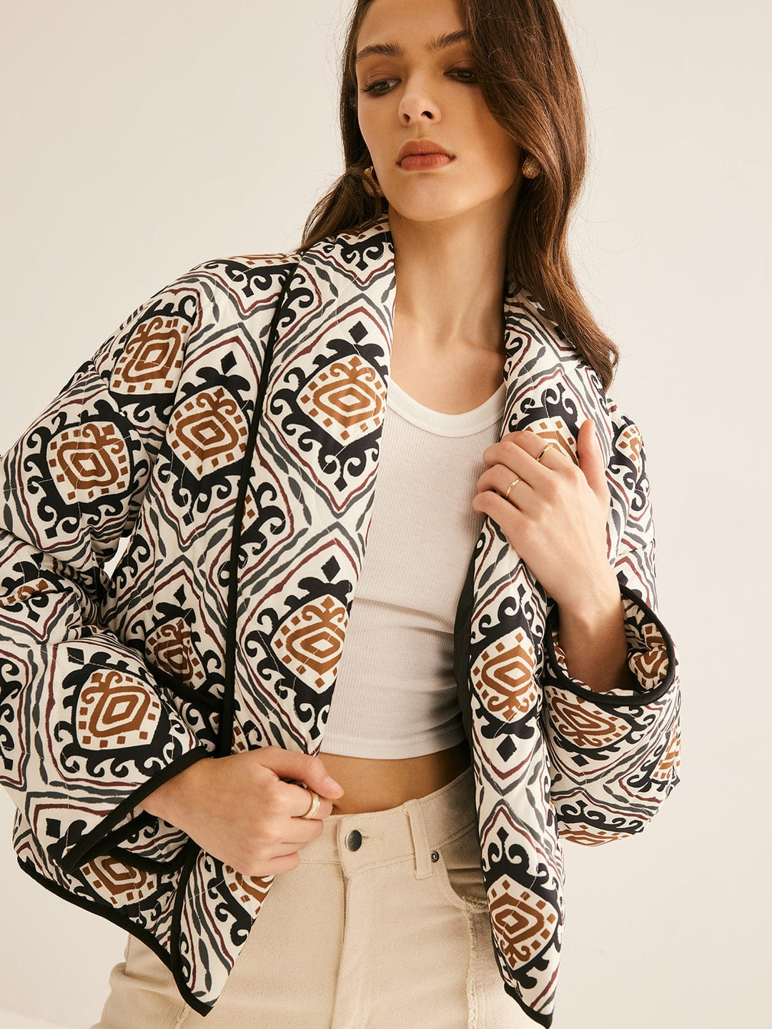 veste ample imprimée de motifs géométriques noir, blanc et brun, manches longues avec bordure noire, portée ouverte sur un haut clair et un pantalon clair, style moderne.